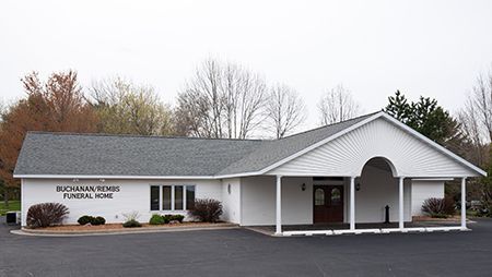 White Buchanan/Rembs Funeral Home building with gray roof and covered entrance.