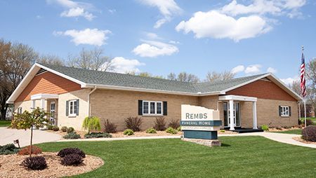 Exterior of a light brown brick building with a green lawn, sign, and American flag. 