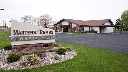 Sign for Martens Rembs Funeral Home in front of the building. Brown brick base, green lawn.