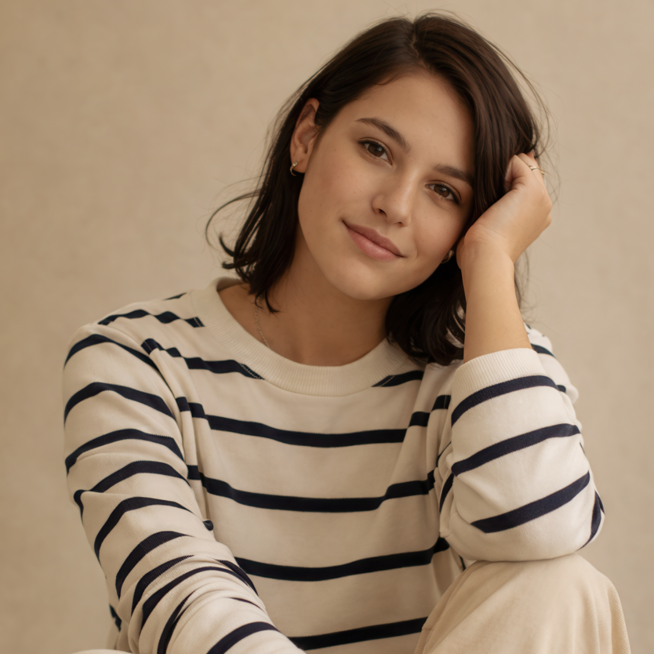 Woman with short brown hair, wearing a striped sweater, resting her chin on her hand, smiling.