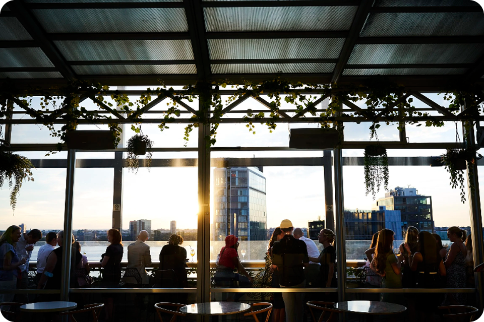 Rooftop bar with a city view at sunset; silhouettes of people enjoying drinks.