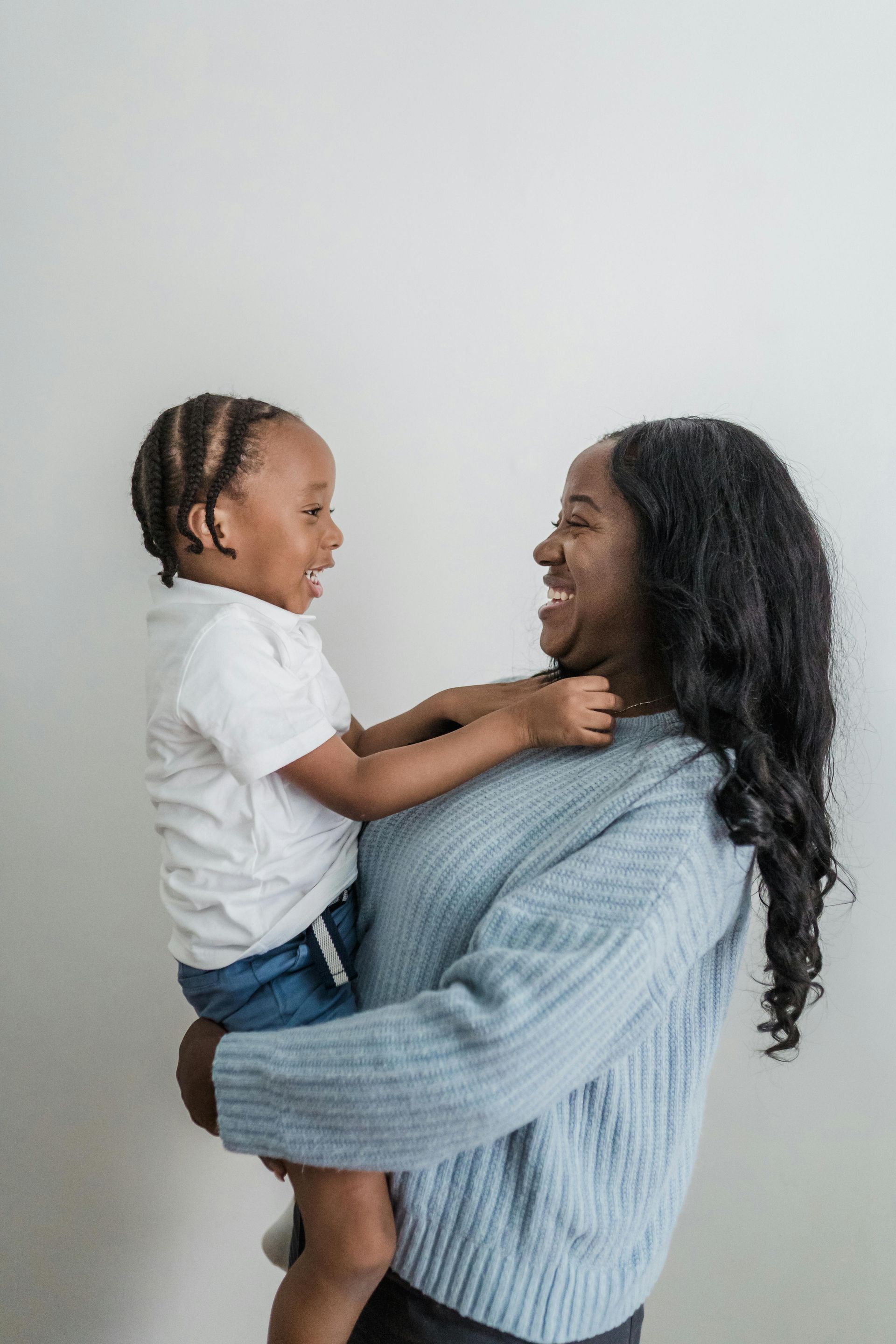 Woman in a blue sweater holds and smiles at a laughing child in a white shirt and blue shorts.