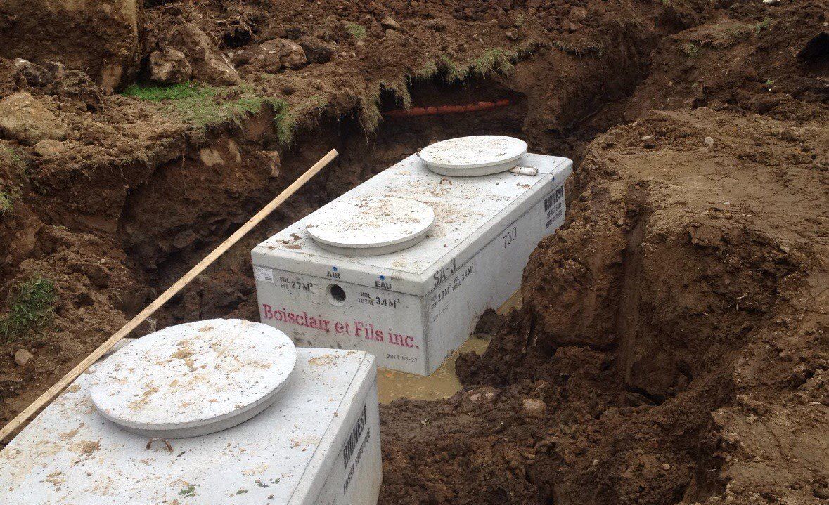 Two concrete septic tanks are sitting in the dirt.