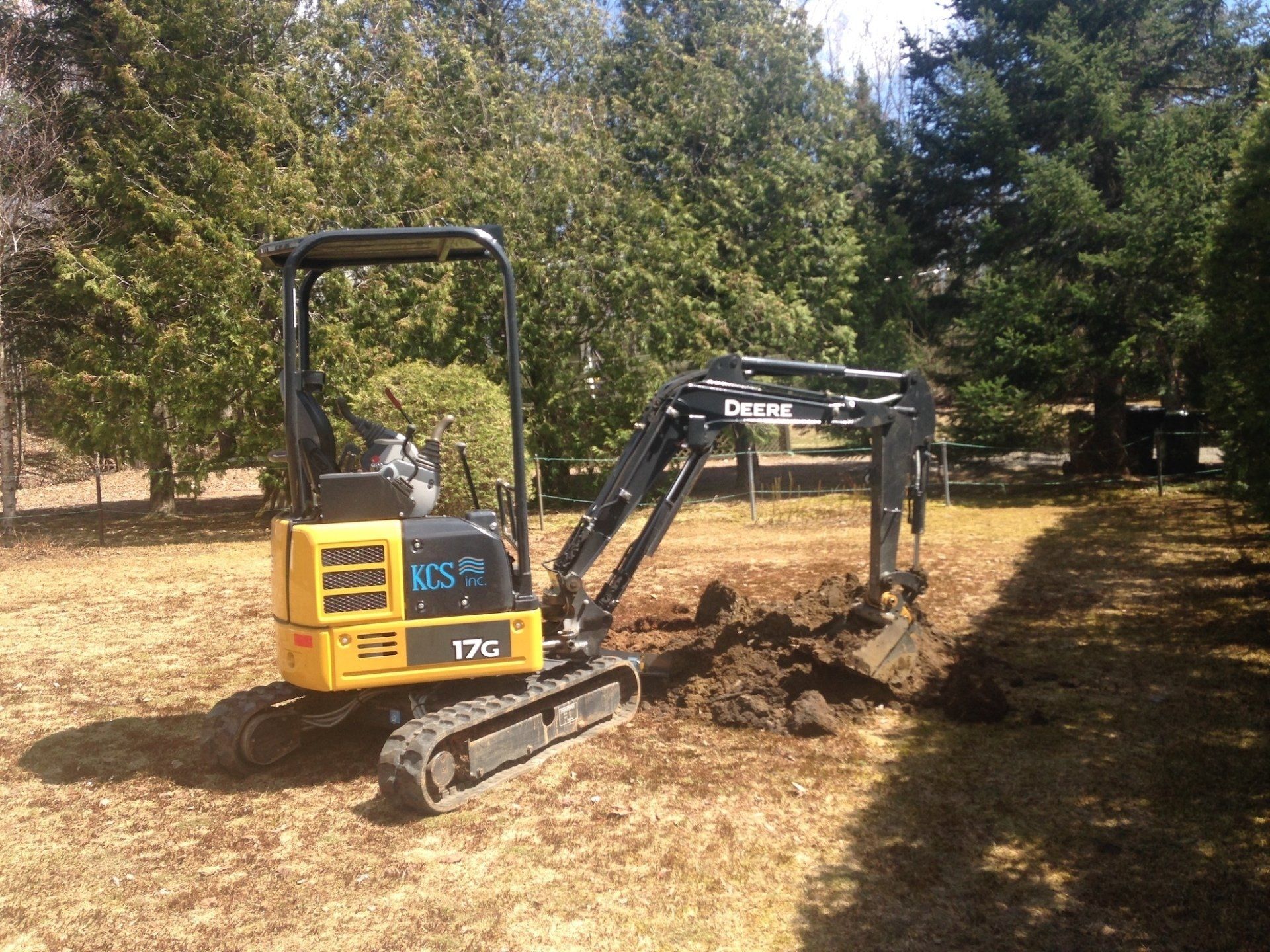 A small yellow excavator is digging a hole in a field.