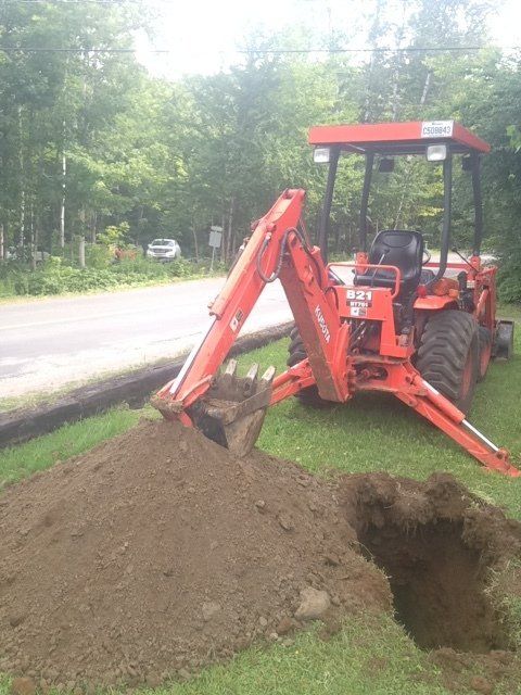 An orange tractor is digging a hole in the grass.