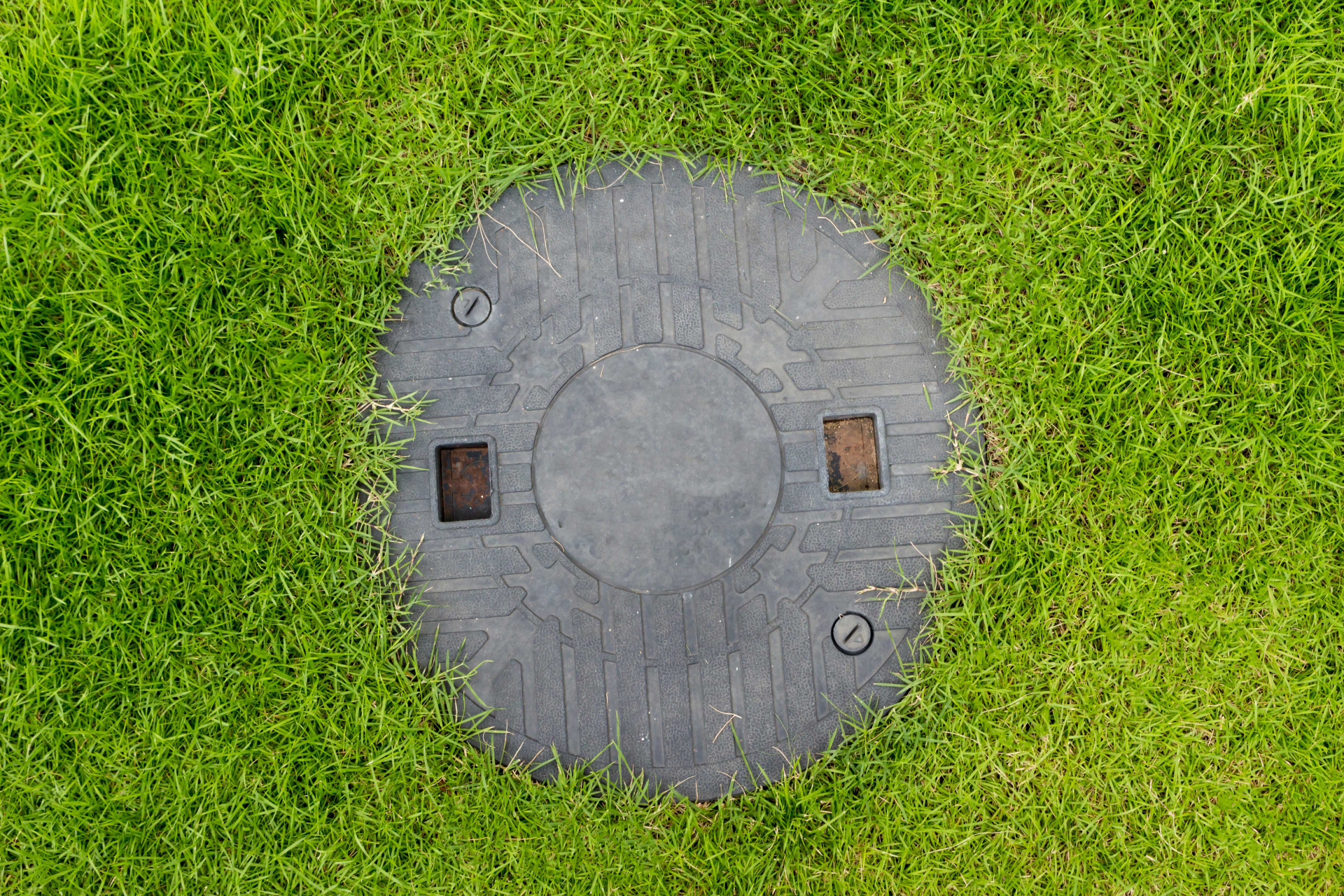 Circular, gray access cover in a grassy lawn.