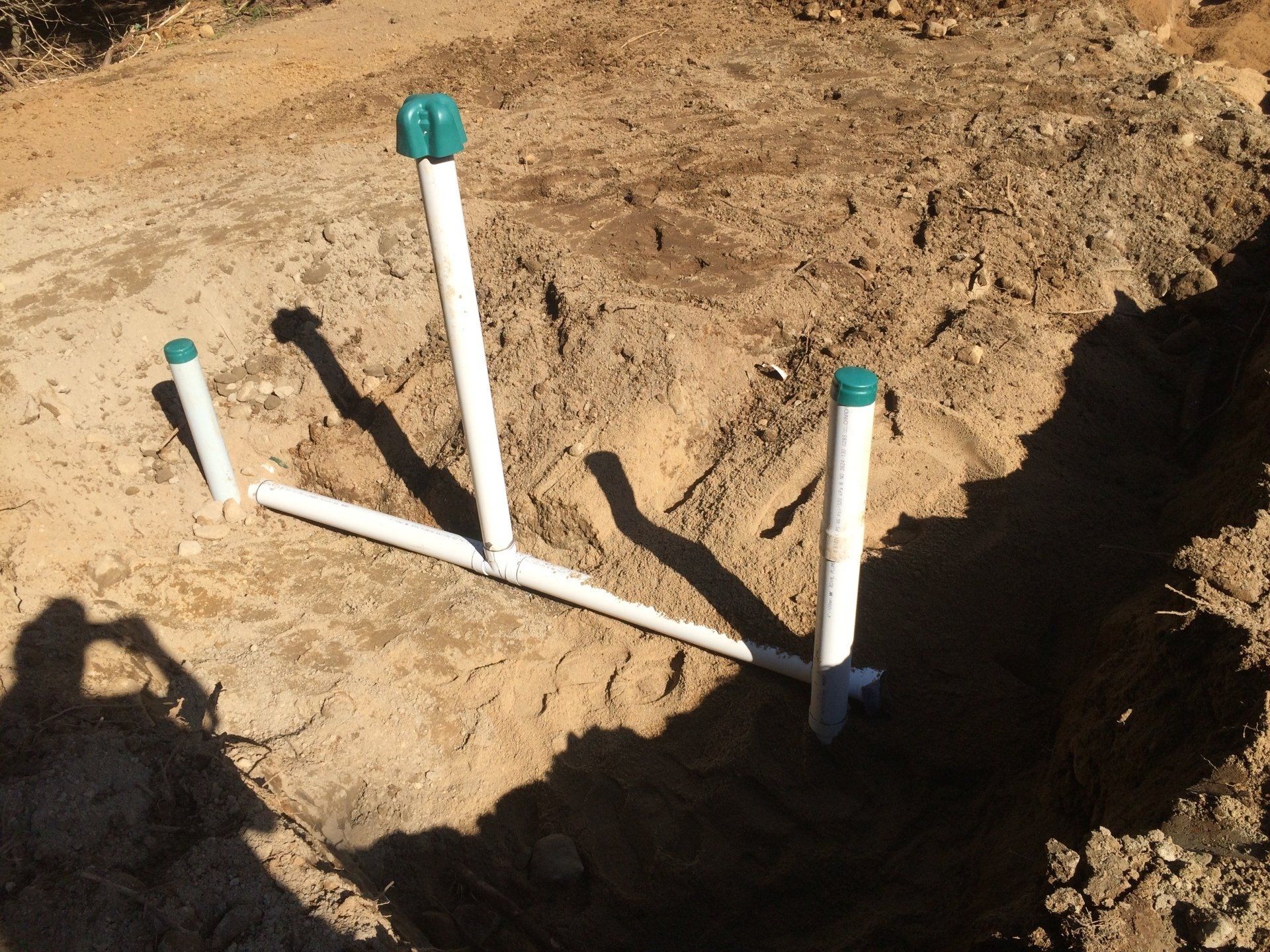 PVC pipes in a sandy trench, three capped vertical pipes connected to a horizontal pipe.