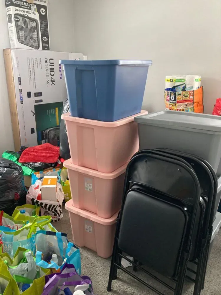 Pink and blue storage bins stacked near black folding chairs; other items in the room.