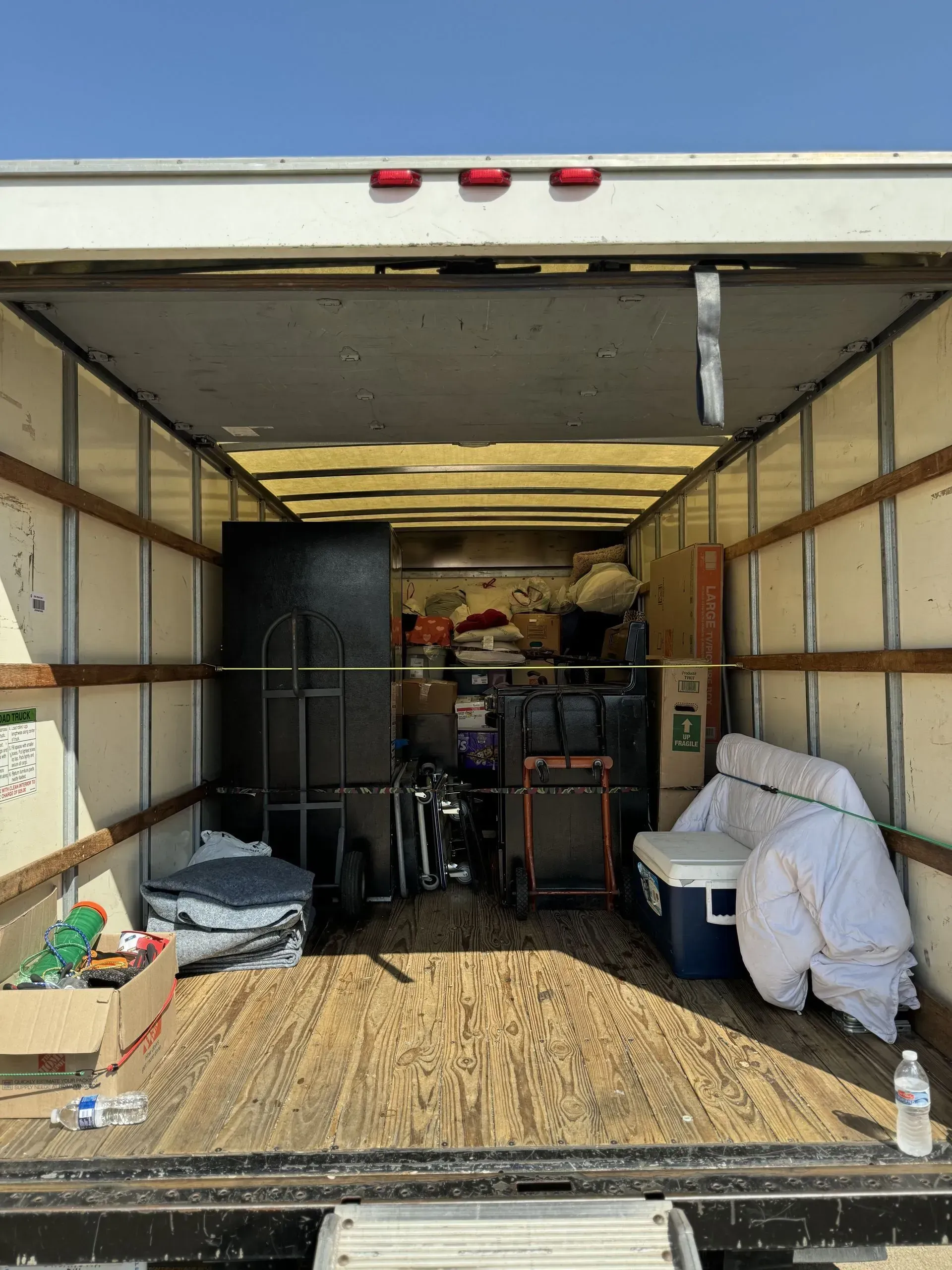 Interior of a moving truck filled with boxes, furniture, and miscellaneous items; viewed from the open back.