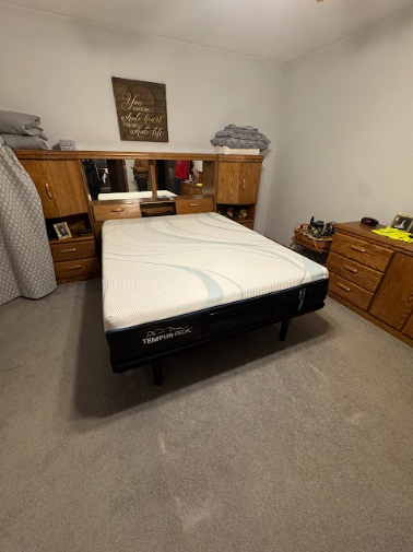 Bedroom with bed, headboard with mirror and cabinets, and wood dresser. Gray carpet.