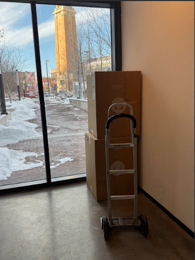 Boxes stacked by a hand truck inside a building, with a winter view through a window.