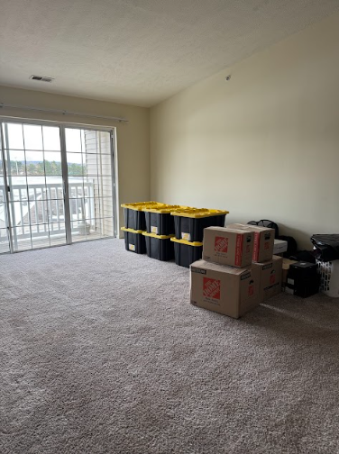 Empty room with carpet and sliding glass door. Boxes and plastic bins sit in the room.