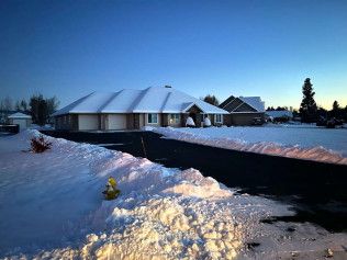 Snow-covered house with a dark driveway against a twilight sky. A yellow fire hydrant is in the foreground.
