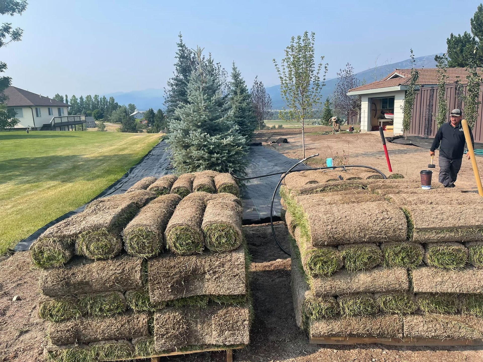 Stacks of sod rolls on pallets, with a worker preparing for installation.