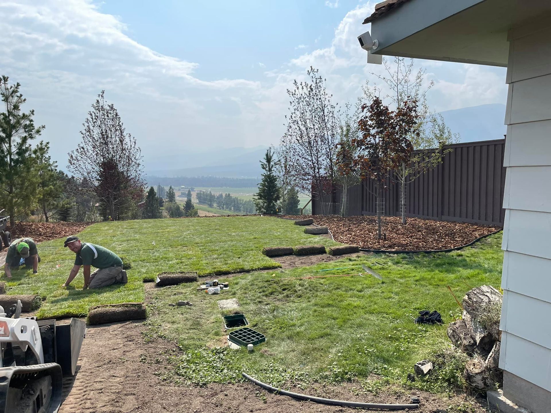 Landscapers laying sod in a yard with a view of mountains under a cloudy sky.