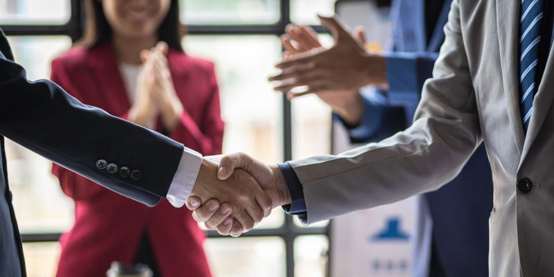 A group of business people are shaking hands in front of a window.