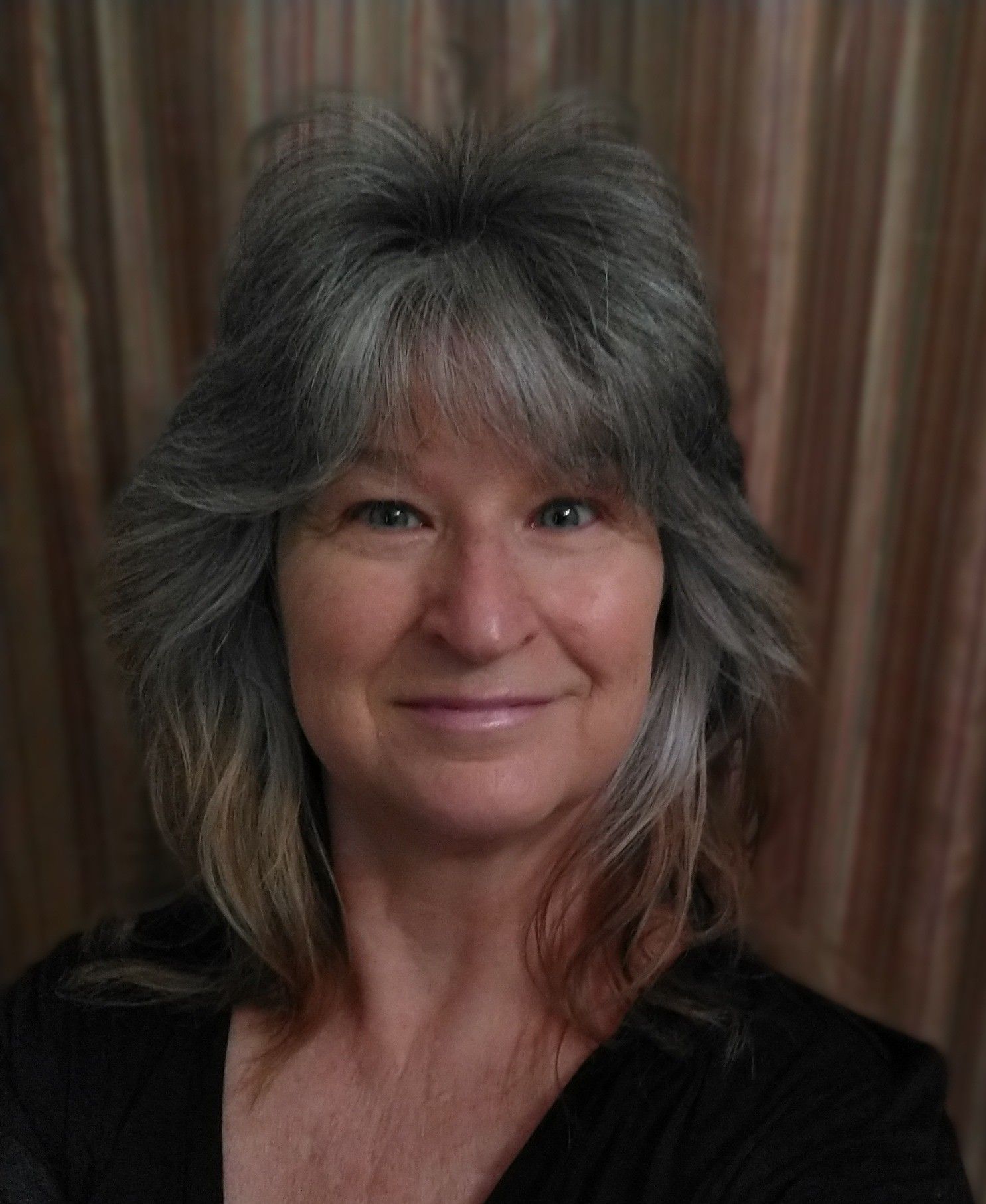 A woman with gray hair and a black shirt is smiling for the camera.