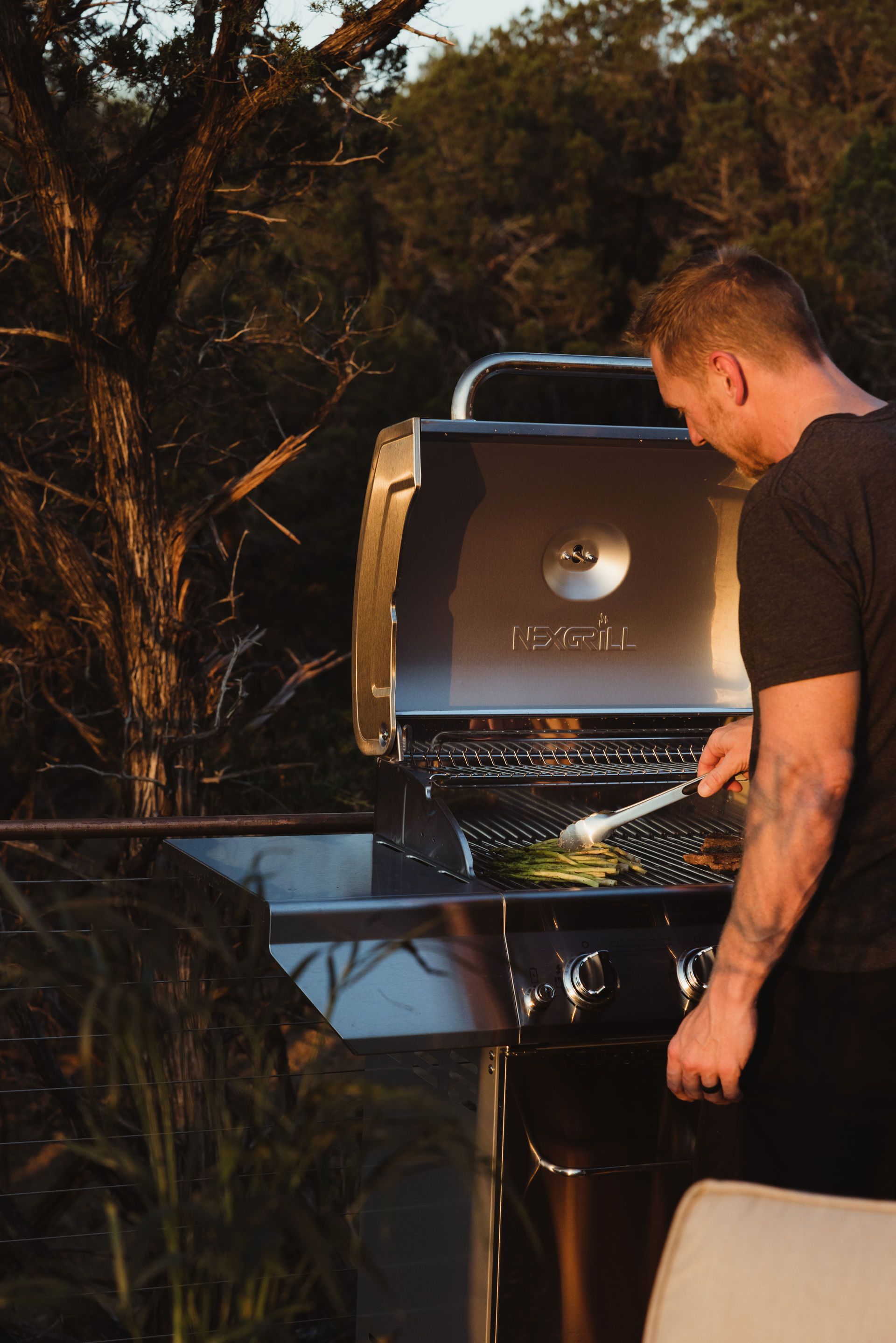 Man grilling food outdoors at sunset.