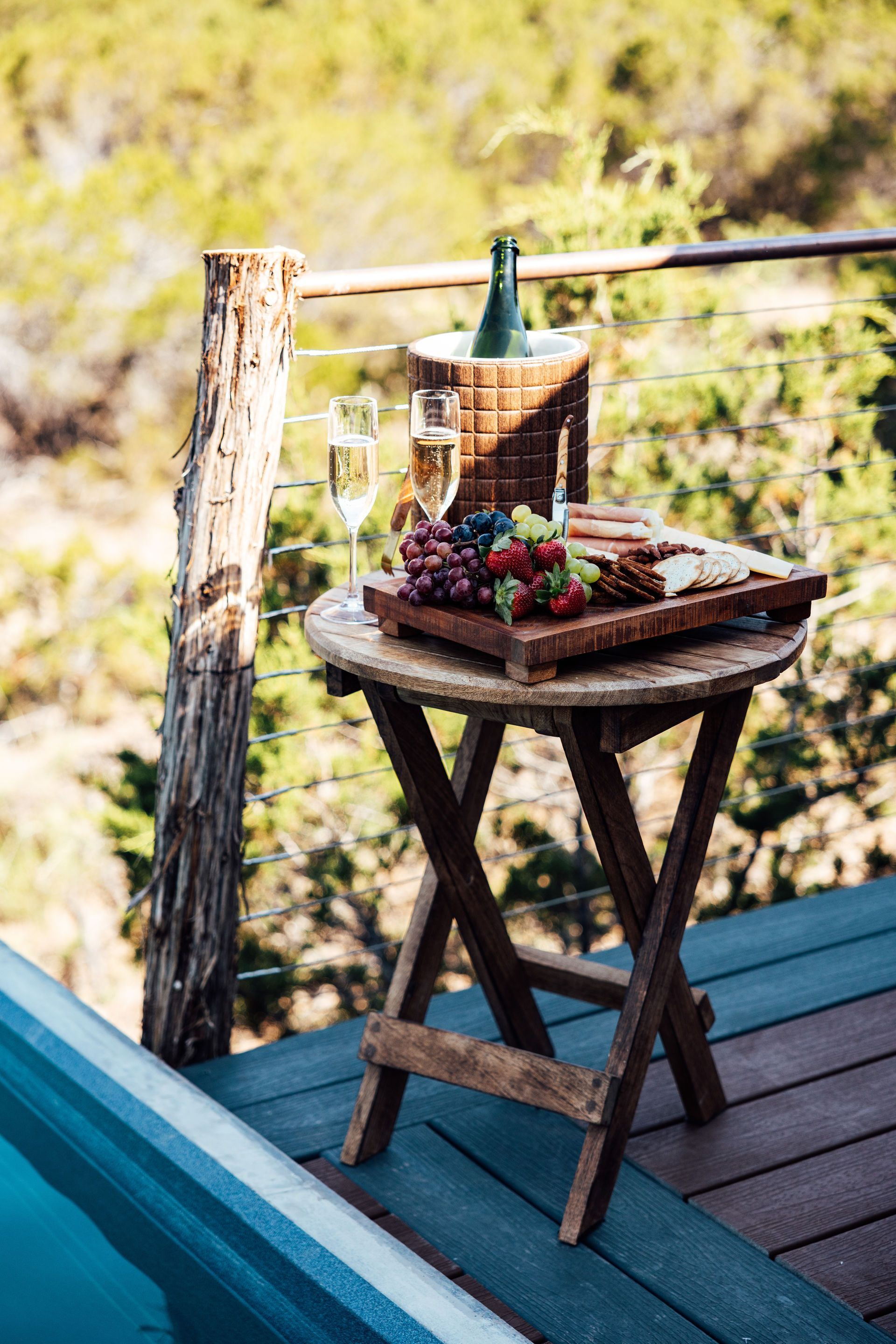 Wooden table with charcuterie, champagne, and a view.