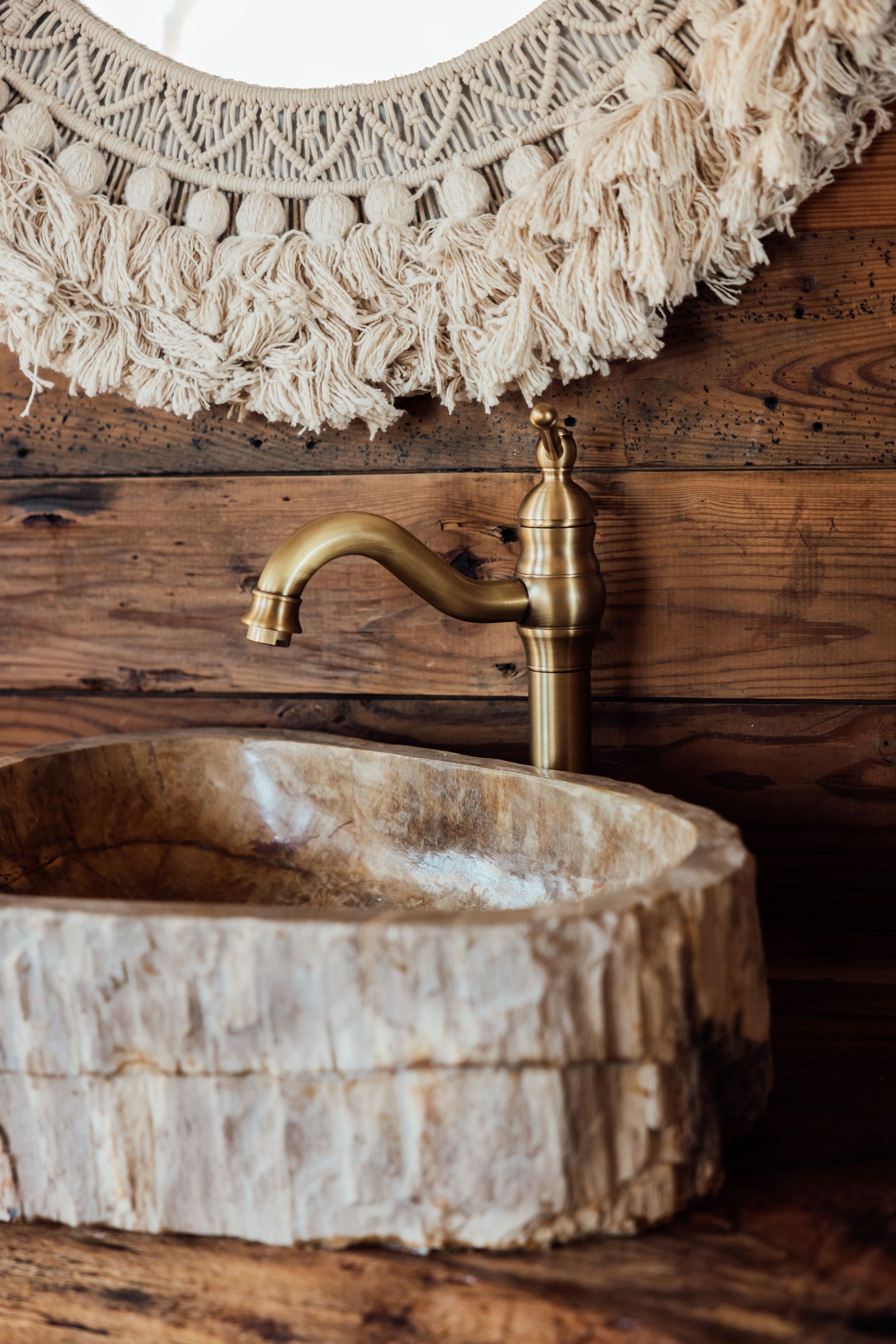 Rustic bathroom sink with bronze faucet against wood paneling, ornate mirror.