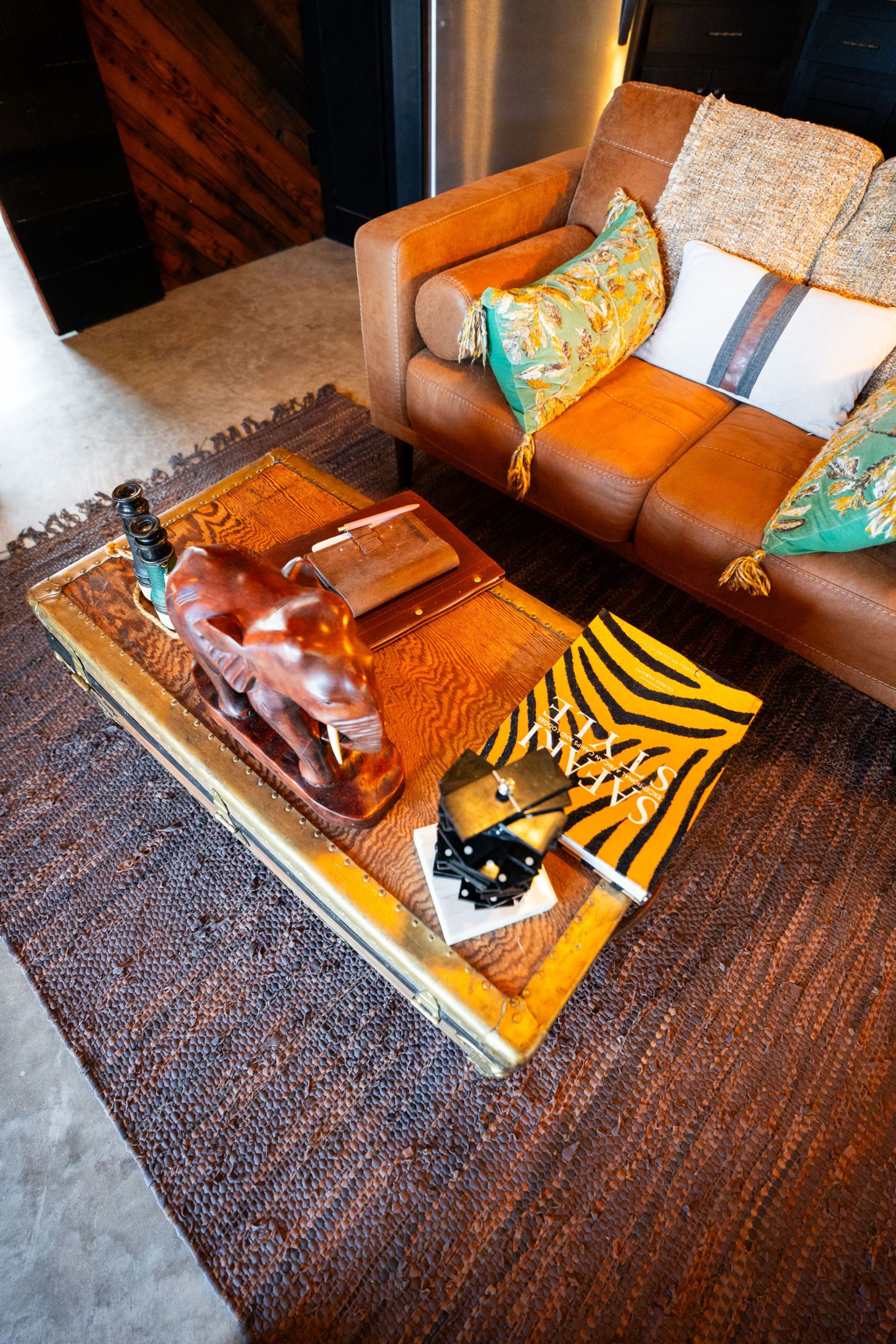 Living room with brown leather couch, gold coffee table with decor, and patterned rug.