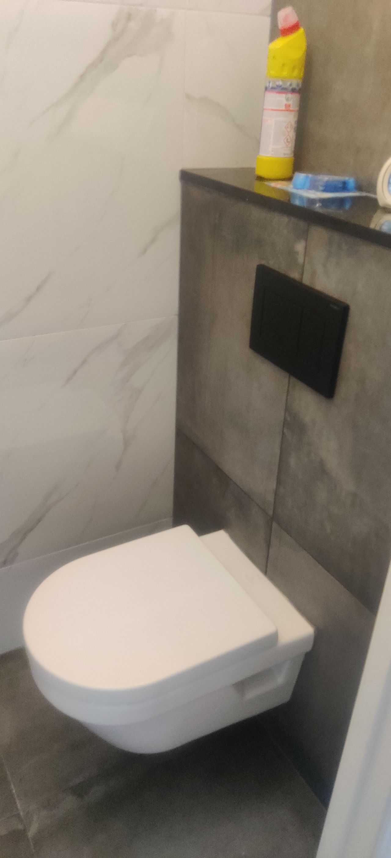 A white toilet is hanging on the wall in a bathroom.