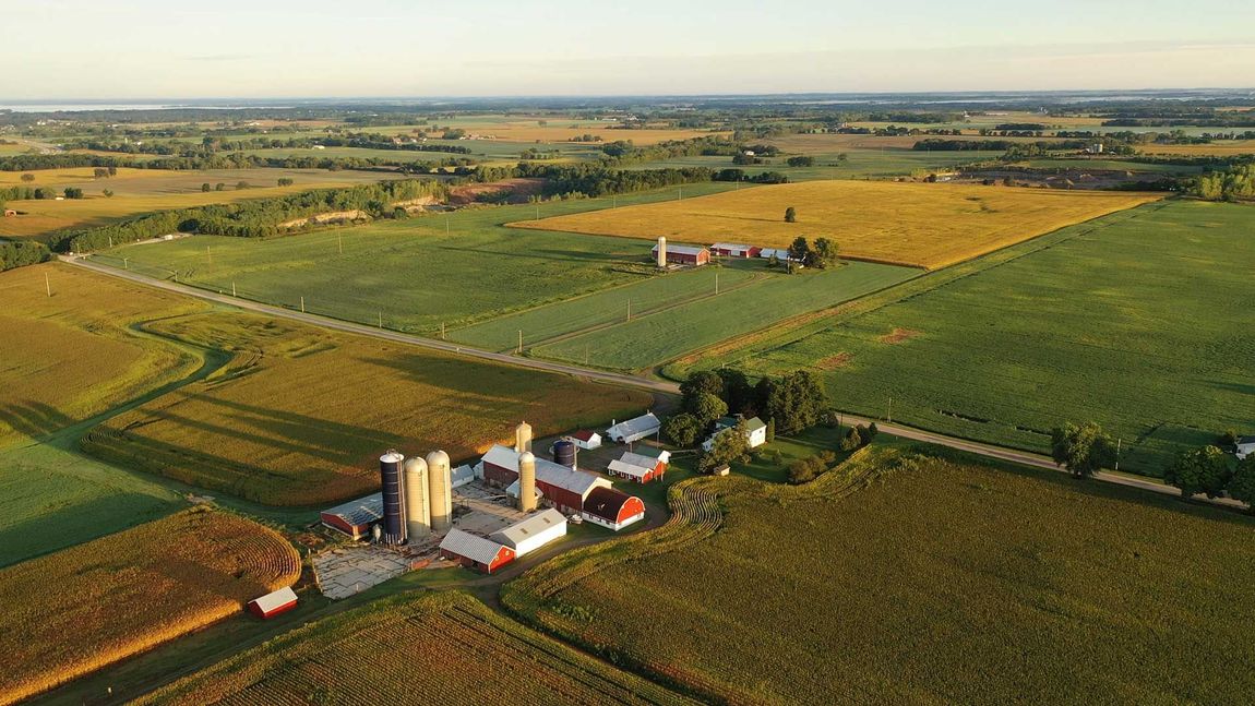 Aerial view of a farm with silos, red barns, and fields of crops under a blue sky.