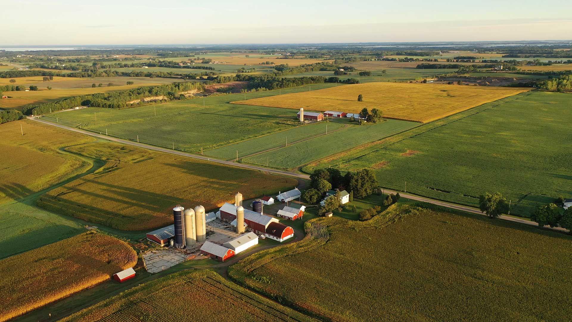 Aerial view of a farm with silos, red barns, and fields of crops under a blue sky.