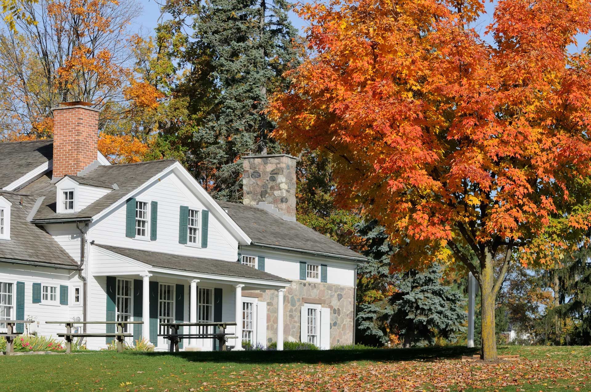 White house with green shutters, surrounded by colorful autumn trees.