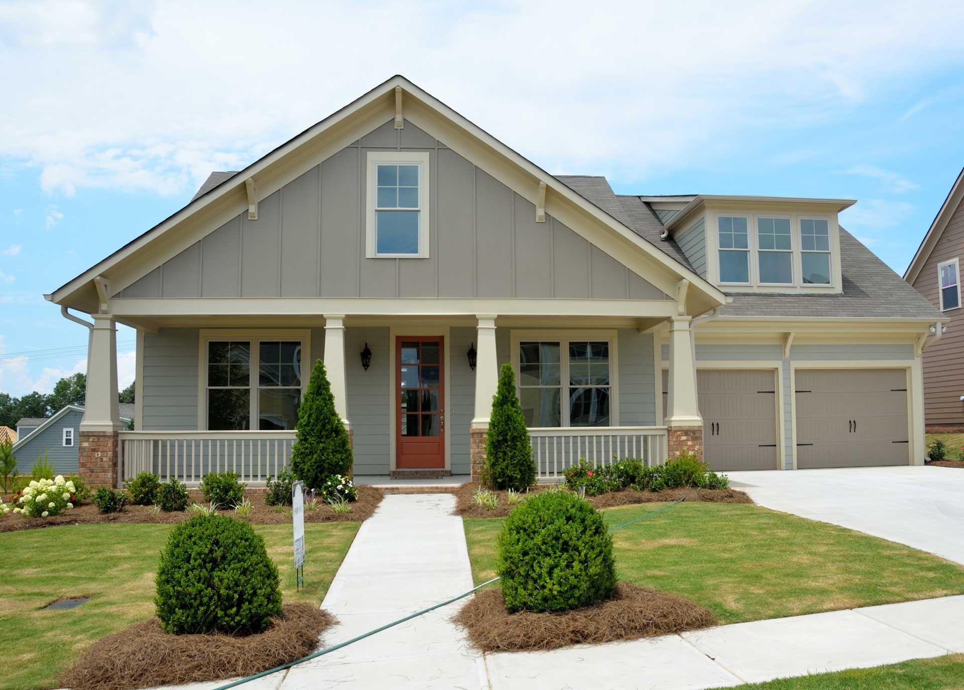 Light gray Craftsman-style house with a porch, brown door, and garage, blue sky in the background.
