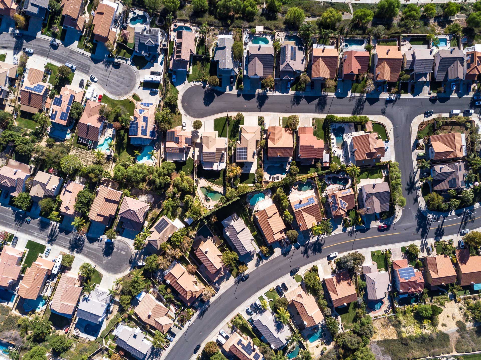 Aerial view of a suburban neighborhood with houses, curved roads, and greenery on a sunny day.