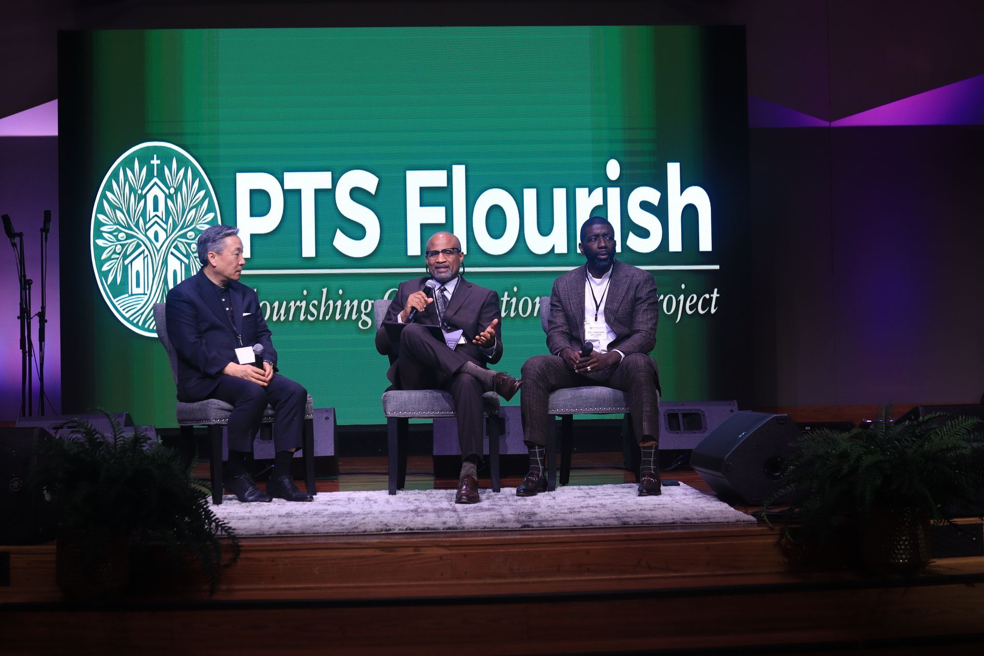 Three men are sitting on a stage in front of a sign that says pts flourish