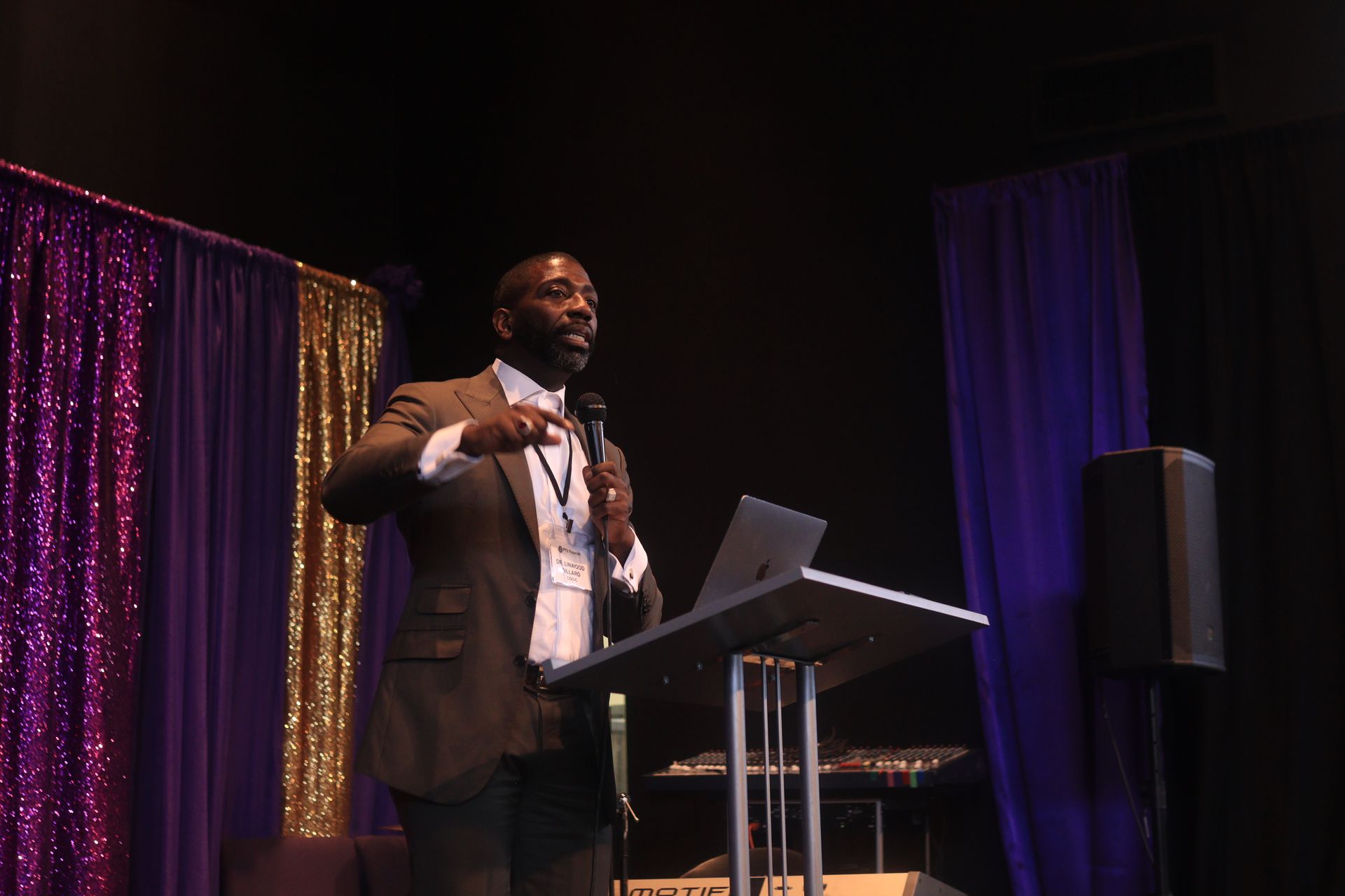 A man in a suit is standing at a podium holding a microphone and a laptop.