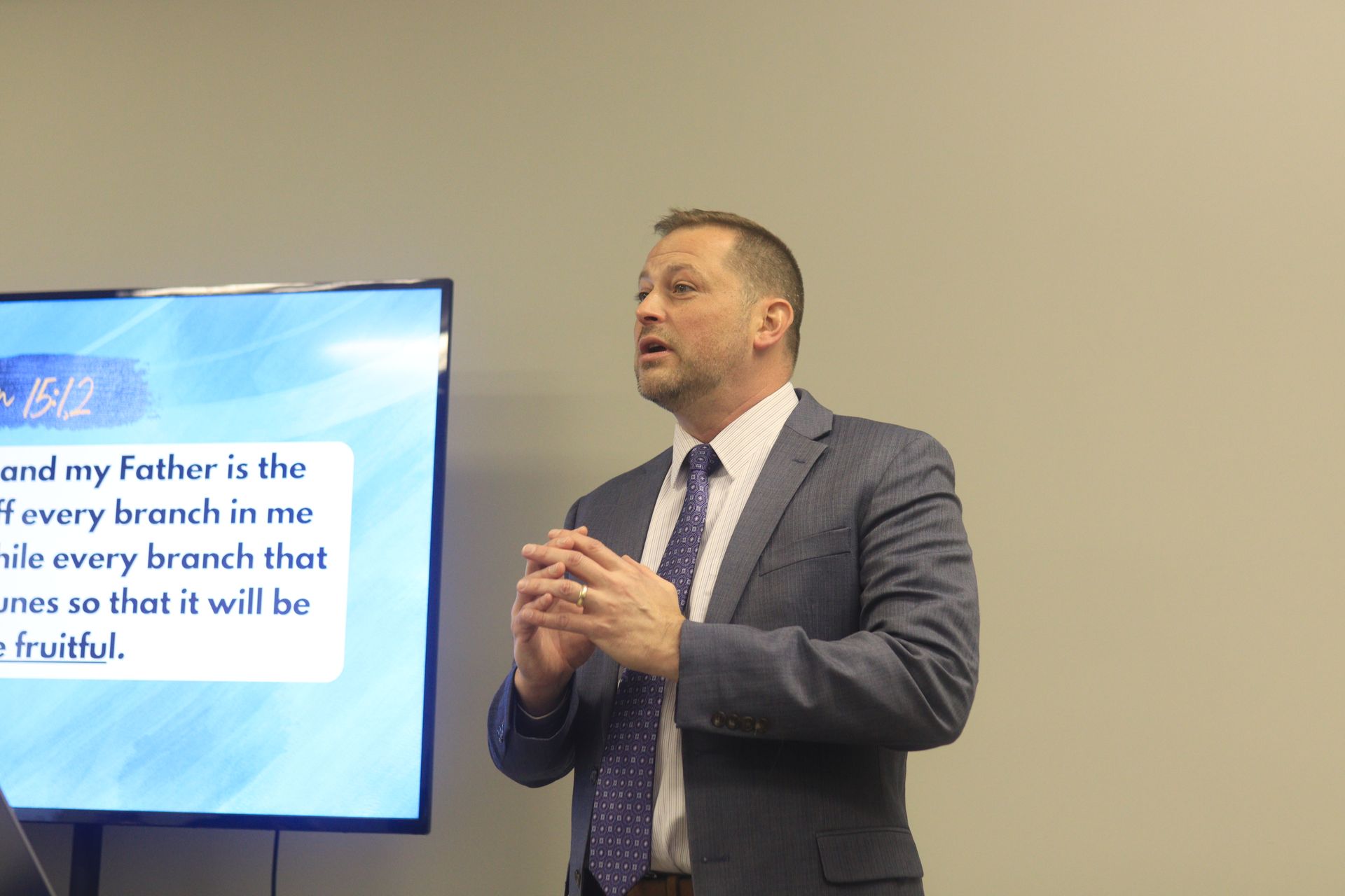 A man in a suit and tie is giving a presentation in front of a screen.