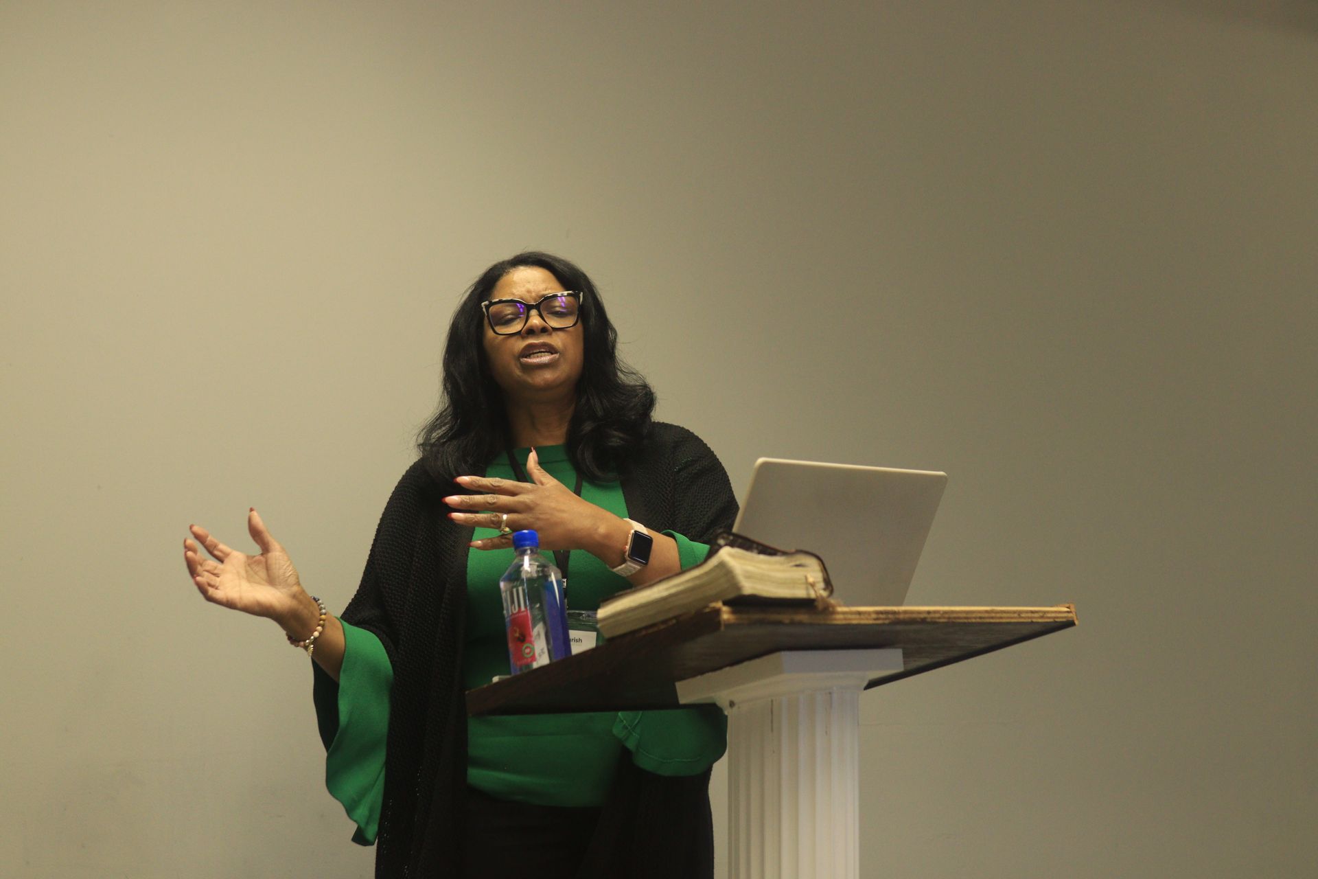 A woman is standing at a podium with a laptop and a bible.