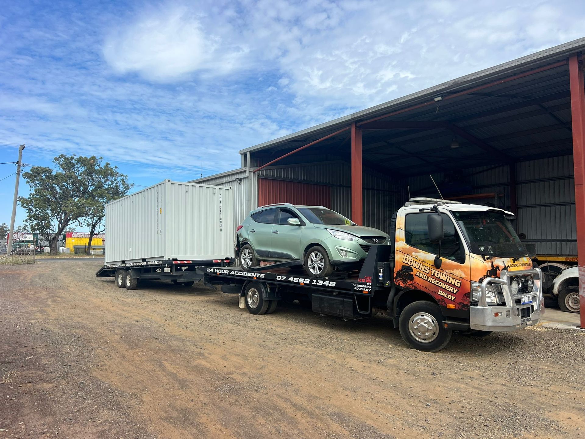 Tow truck hauling a green SUV and a white shipping container beside a warehouse on a dirt lot.  — Downs Towing & Recovery Service in Chinchilla, QLD