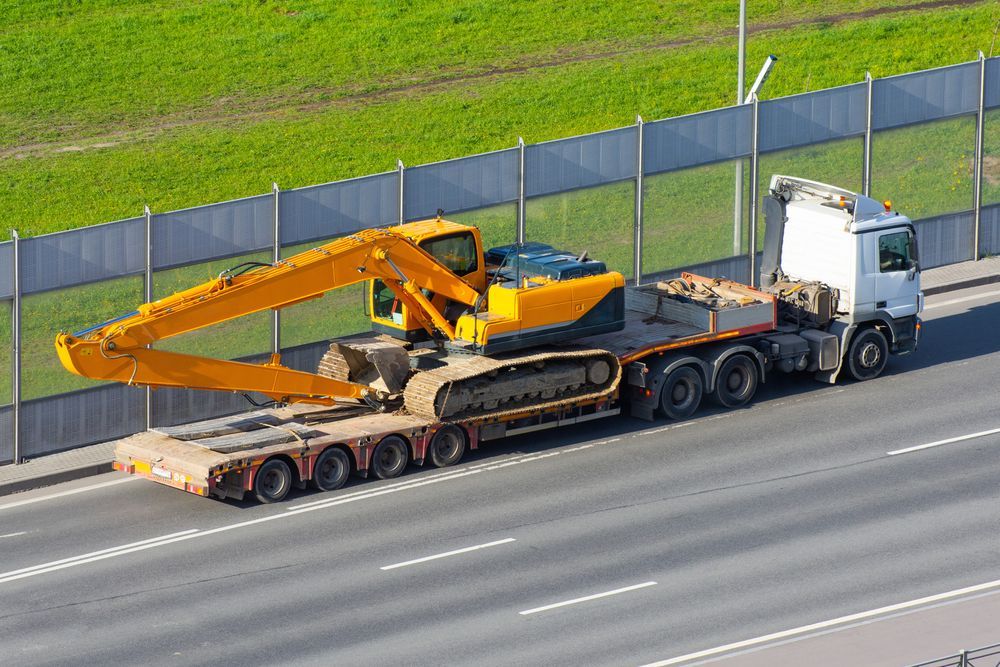 Yellow Excavator on a Flatbed Trailer Being Transported on a Highway — Downs Towing & Recovery Service in Chinchilla, QLD