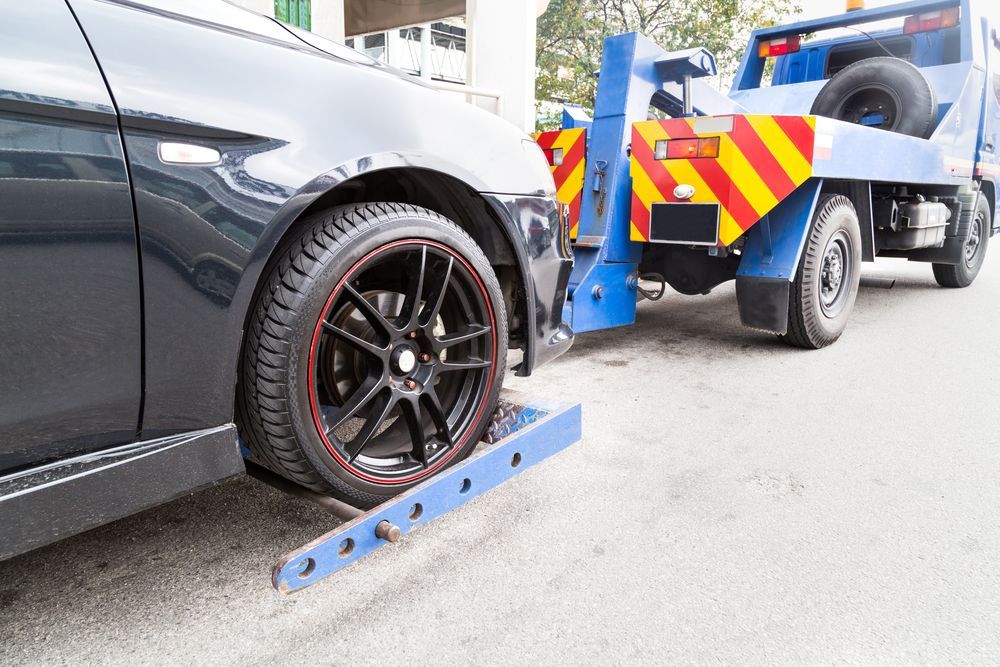 Black Car Being Towed by a Blue Tow Truck on a Paved Road — Downs Towing & Recovery Service in Moonie, QLD