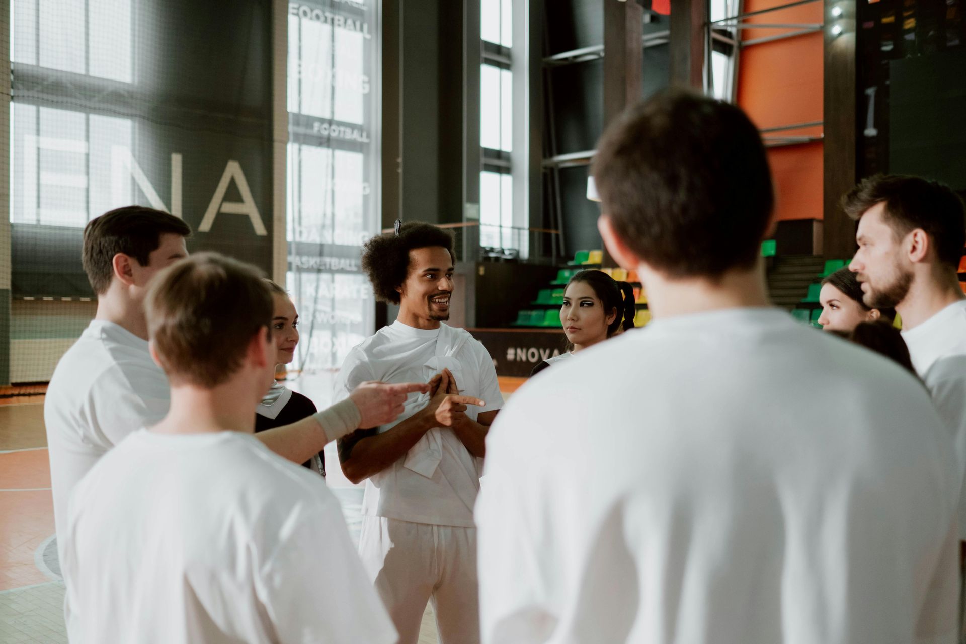 People in white shirts standing in a circle, talking in a gym setting.