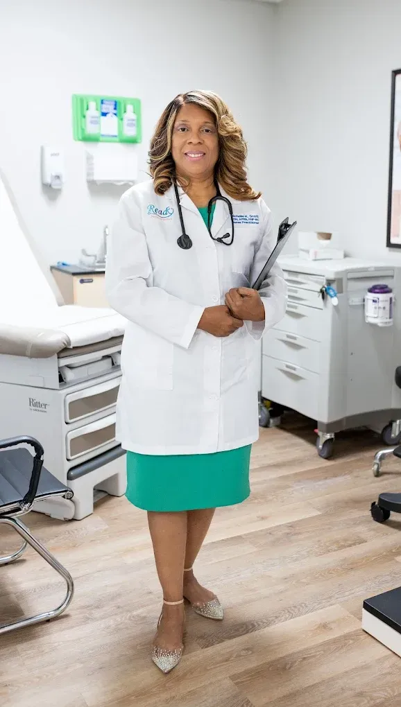 A woman in a lab coat and green dress is standing in a doctor 's office.