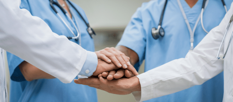 A group of doctors and nurses are putting their hands together.