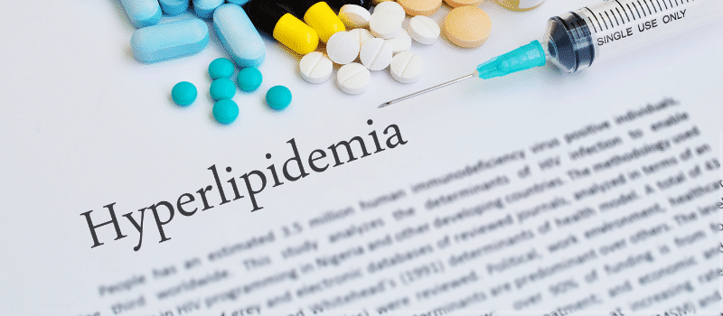 A syringe and pills are on a piece of paper that says hyperlipidemia.