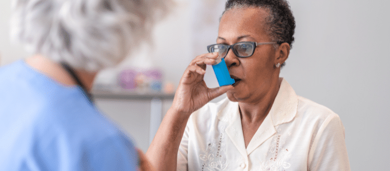 An older woman is using an inhaler to treat her asthma.
