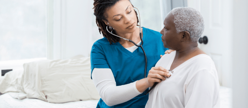 A nurse is listening to an older woman 's heartbeat with a stethoscope.