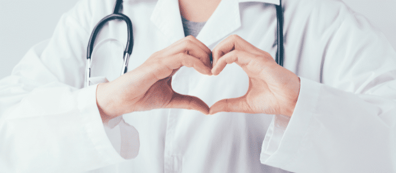 A doctor is making a heart shape with her hands.