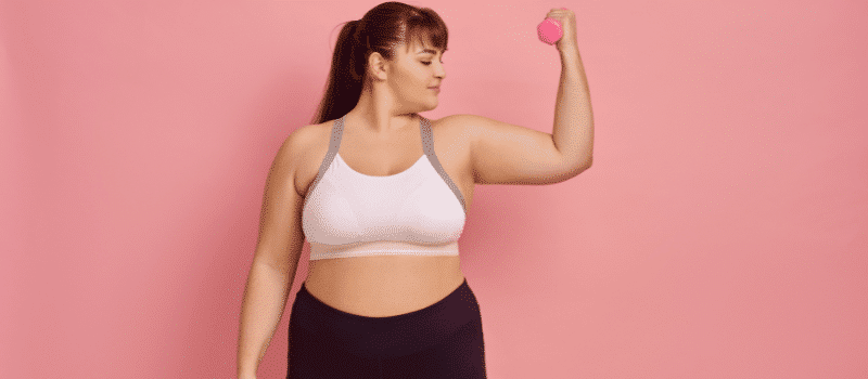A woman is lifting a pink dumbbell on a pink background.