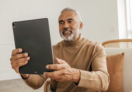 An older man is sitting in a chair holding a tablet computer.