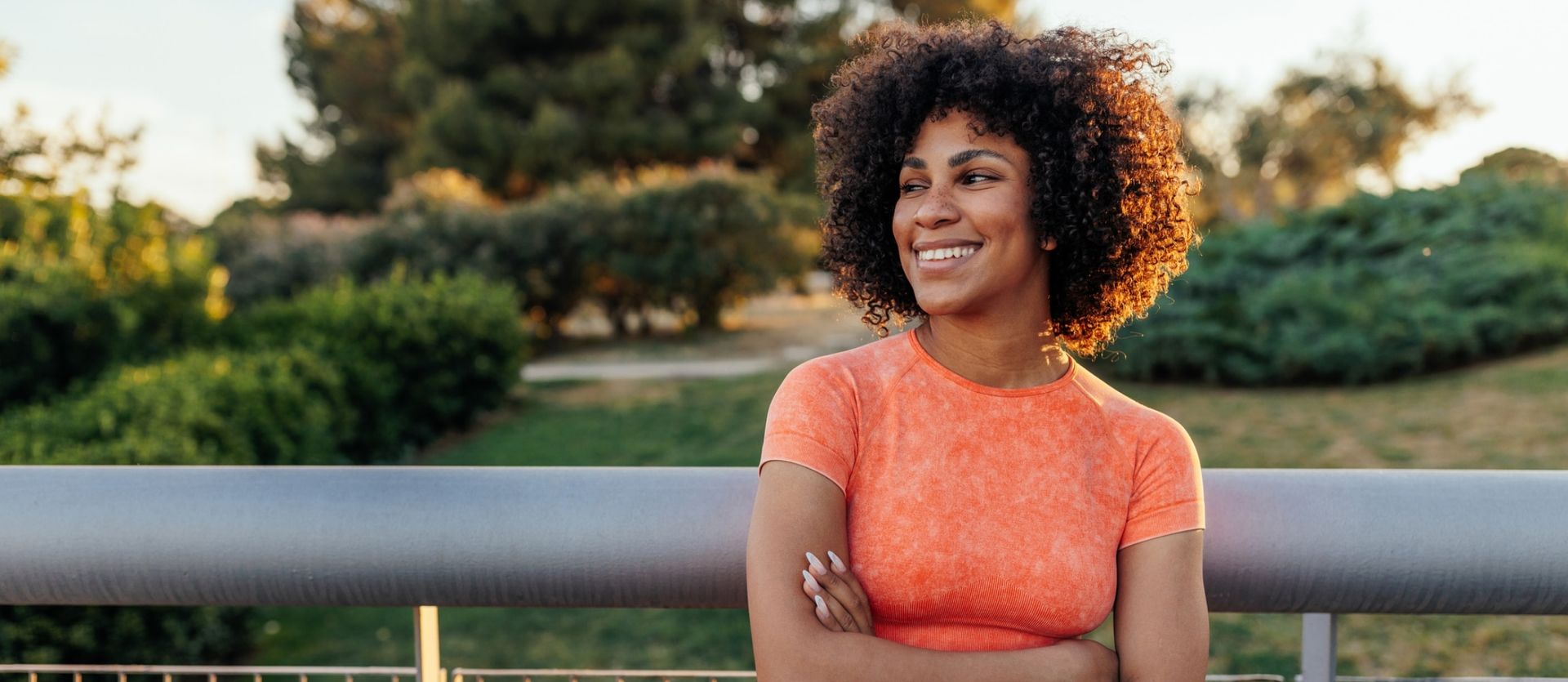 A woman is standing on a bridge with her arms crossed and smiling.