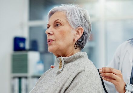 An elderly woman is being examined by a doctor with a stethoscope.