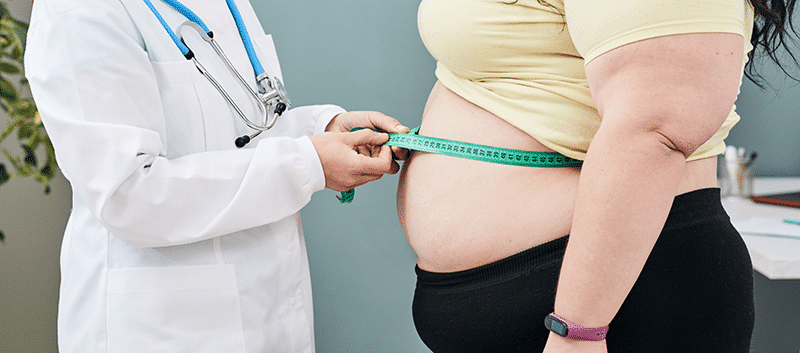 A doctor is measuring a woman 's waist with a tape measure.